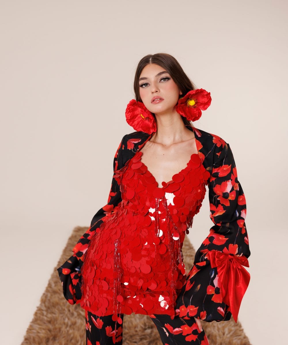 Kırmızı kasnak payetlerin ışıltısını ve ipek kumaşın akışkan dokusunu sergileyen, İspanyol kollu Soul of Leila Alhambra Ember couture takım yakından görünüm.